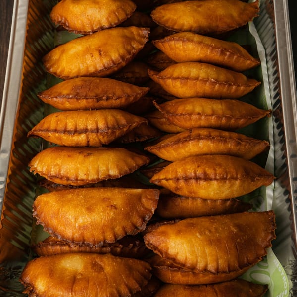Golden-brown Venezuelan empanadas, arranged in rows inside a silver foil container lined with green paper.