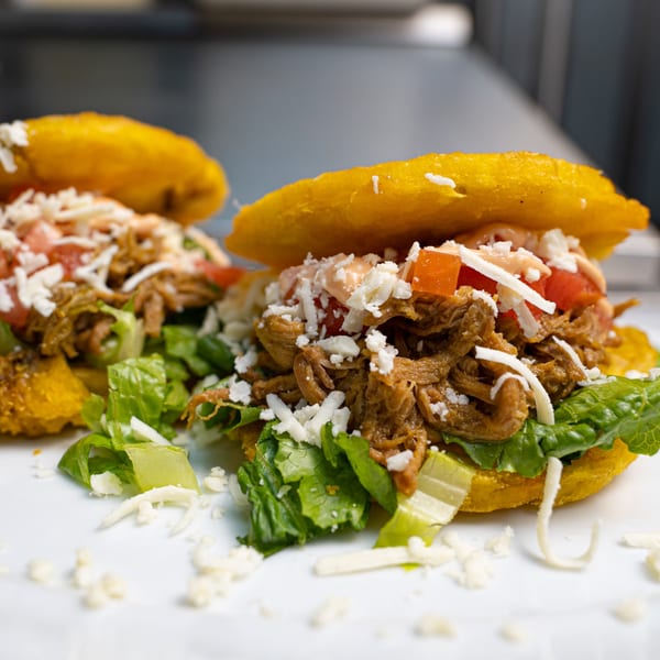 Two Venezuelan arepas filled with shredded beef, lettuce, diced tomatoes, cheese, and sauce.