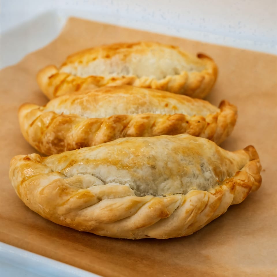 Three golden-brown Venezuelan empanadas with crimped edges, resting on a sheet of parchment paper.