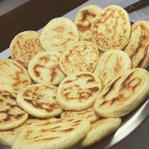 A close-up of a platter filled with many golden-brown, freshly grilled Venezuelan arepas.